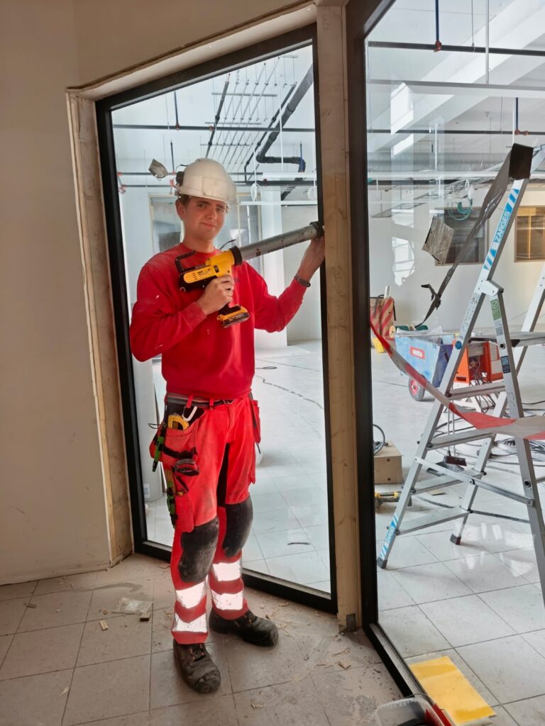 Thomas Torp, lærling hos Ecosør, monterer et glassfelt på en byggeplass innendørs.