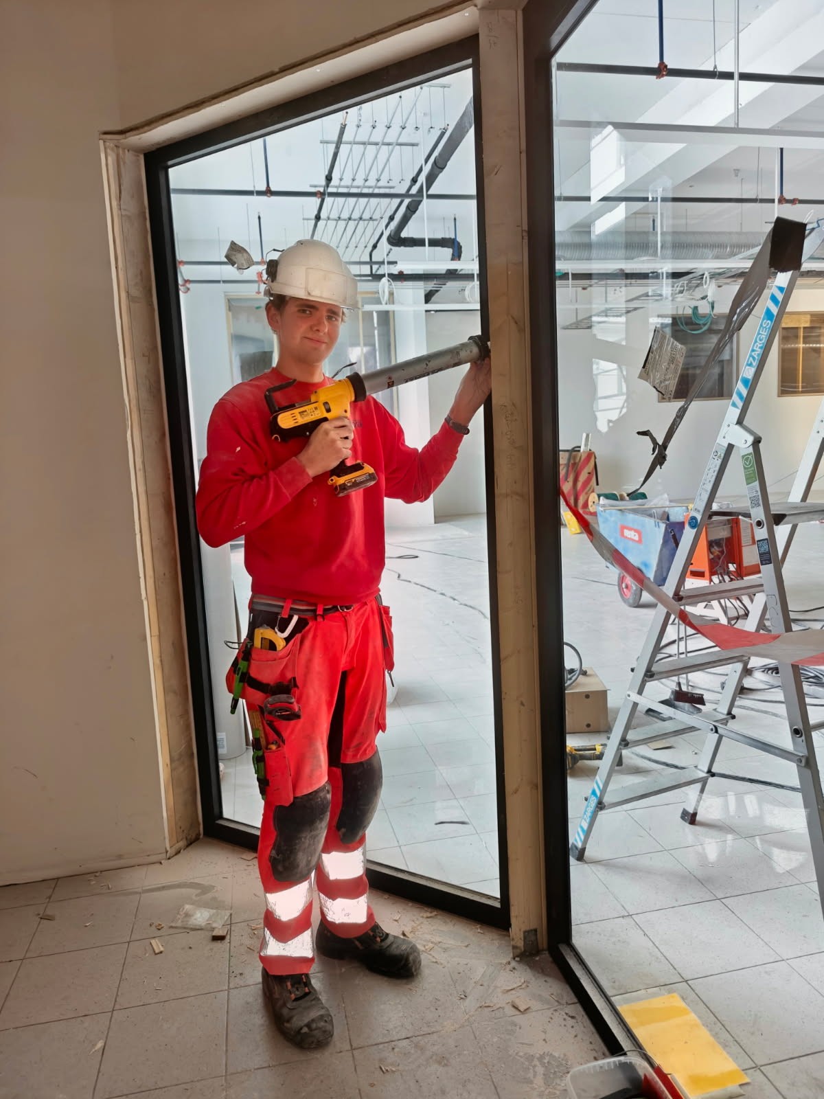 Thomas Torp, lærling hos Ecosør, monterer et glassfelt på en byggeplass innendørs.